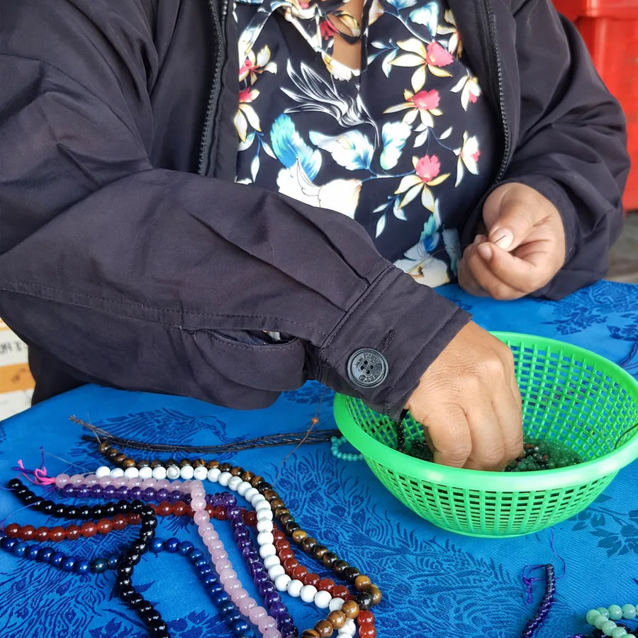 Ses mains puisent des perles dans une corbeille, un fil tendu au-dessus